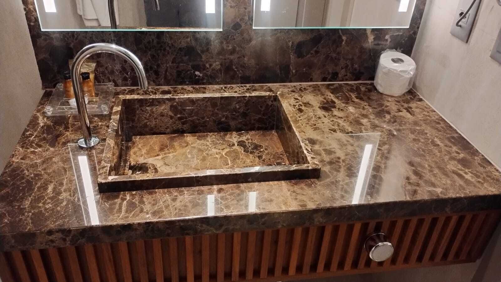 A bathroom with a marble sink, a glass shower enclosure, and a wooden vanity.