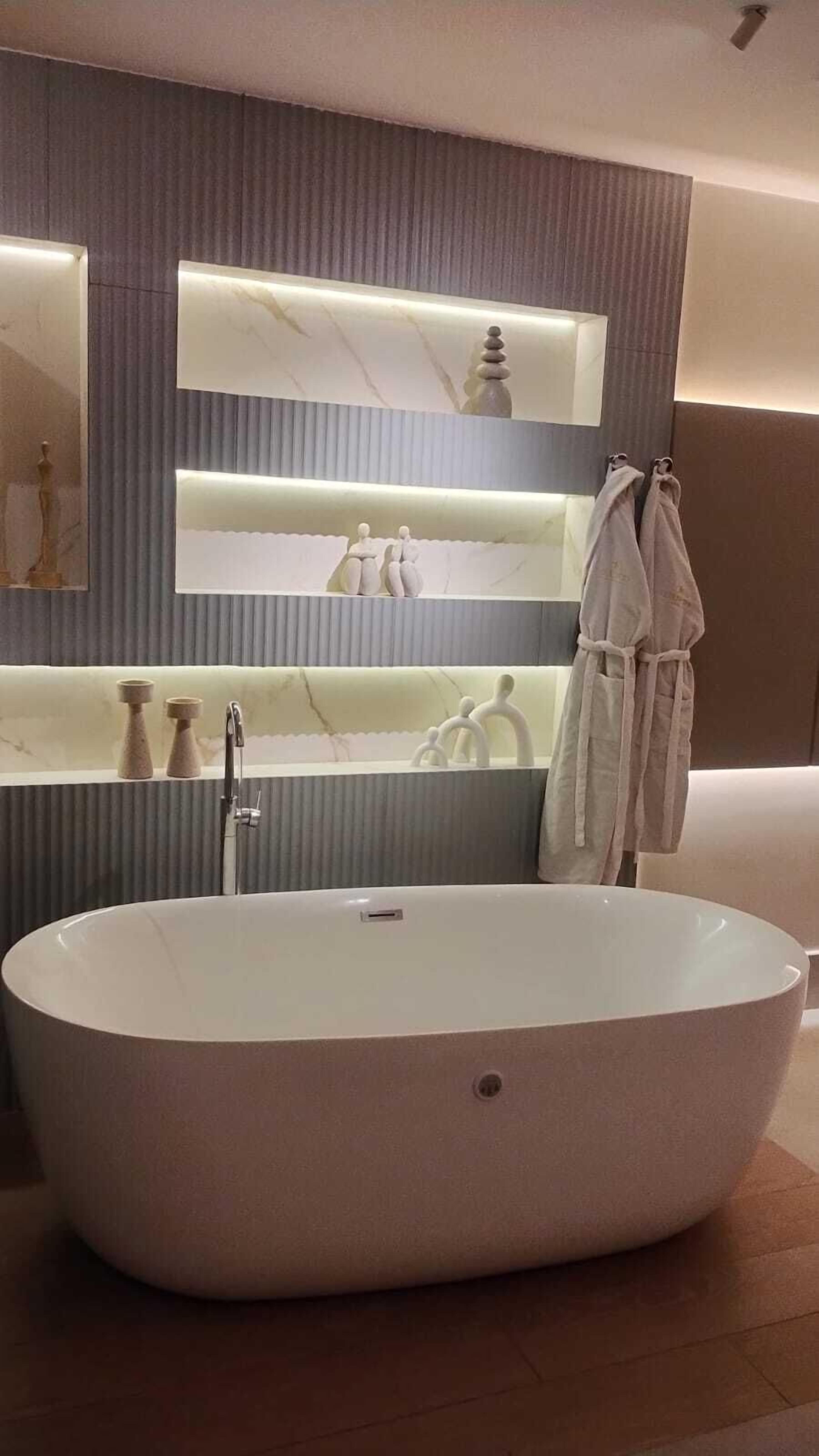 A modern bathroom with a freestanding bathtub, a large mirror, and a shelf with toiletries.
