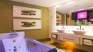 A modern bathroom with a large bathtub, two sinks, a mirror, and a television. - Hotel Corinto (Rio de Janeiro)