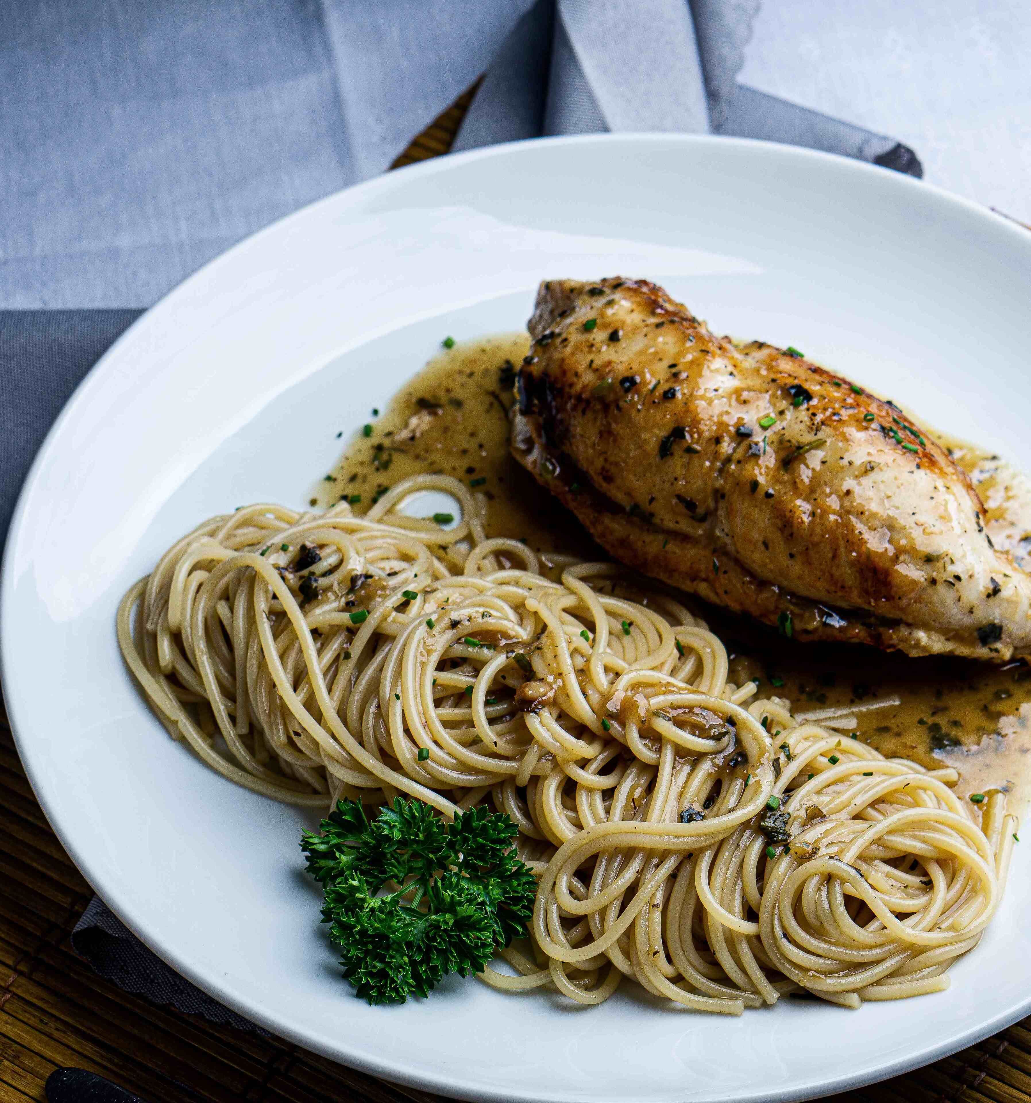Um prato de espaguete com um pedaço de frango grelhado e um toque de salsa.