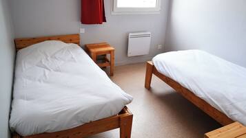 Ein Zimmer mit zwei hölzernen Betten, einem kleinen Holztisch, einem roten Vorhang und einem Fenster mit Tageslicht.
