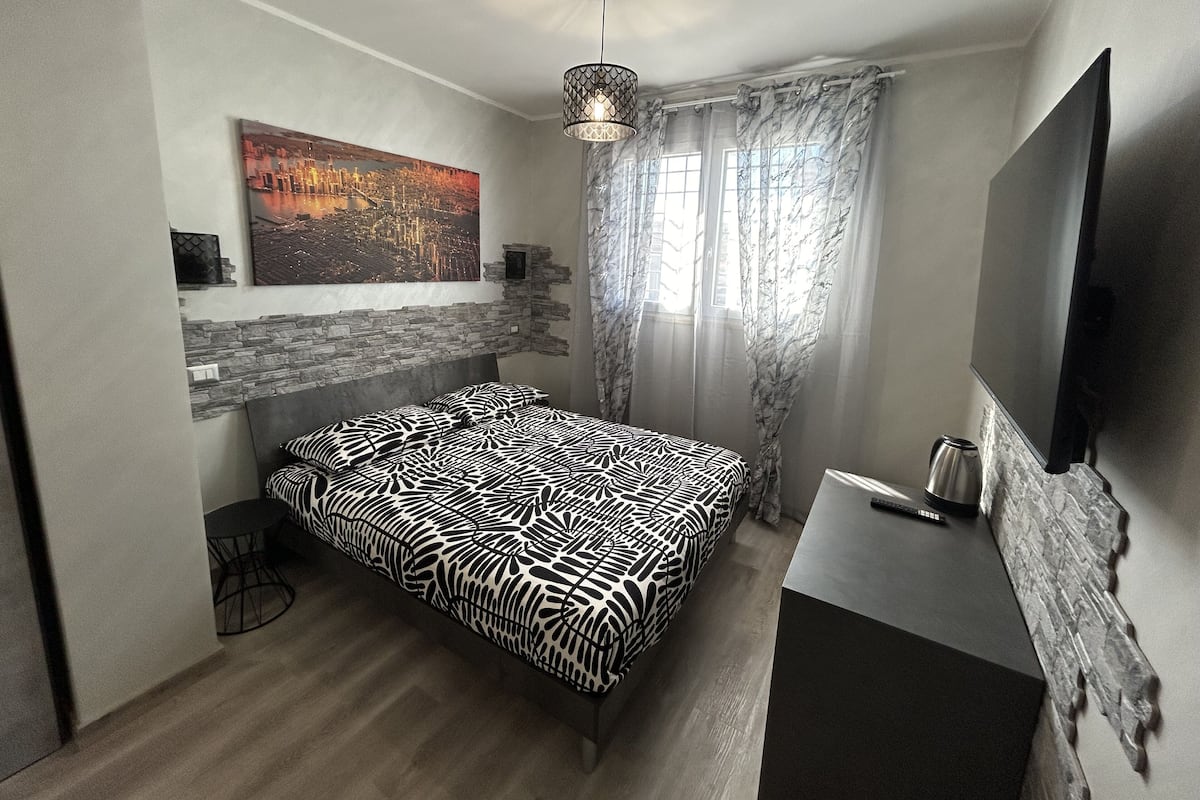 A modern bedroom with a bed, a TV, a painting, and a window with curtains.