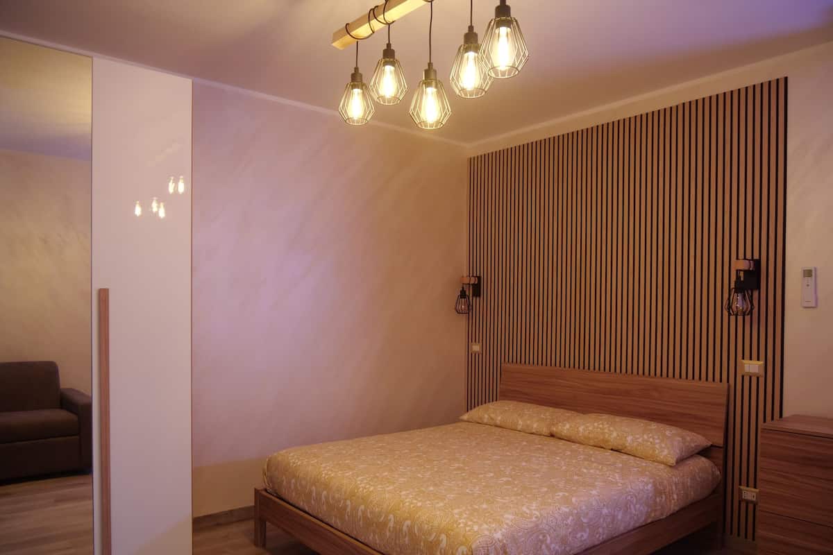 A bedroom with a wooden bed, a nightstand, a dresser, and a hanging light fixture.
