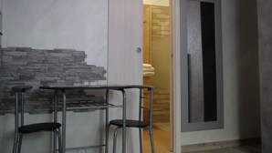 A room with a stone accent wall, a small bar area with stools, and a door leading to a bathroom with a wooden shower enclosure. - Our Guest House (Fiumicino)