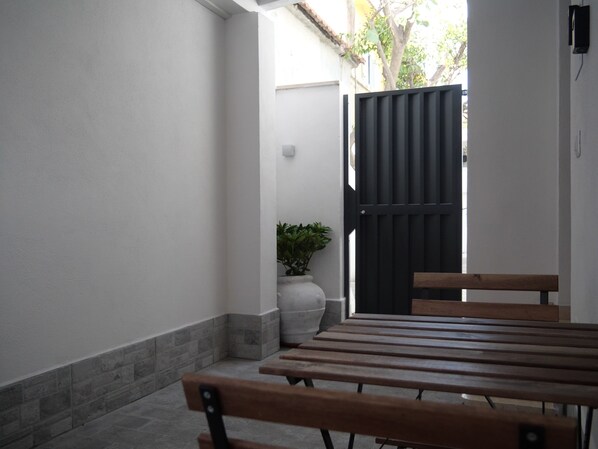 A patio with a wooden table and benches, a potted plant, and a black gate.