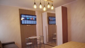 A modern hotel room with a wooden floor, a bed with a patterned bedspread, a sofa, a small round table with chairs, and a wall-mounted TV displaying various streaming services. - Our Guest House (Fiumicino)