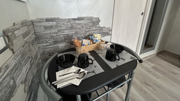 A small round table with a black tablecloth, a tray of bread, a coffee maker, and a mug. - Our Guest House (Fiumicino)