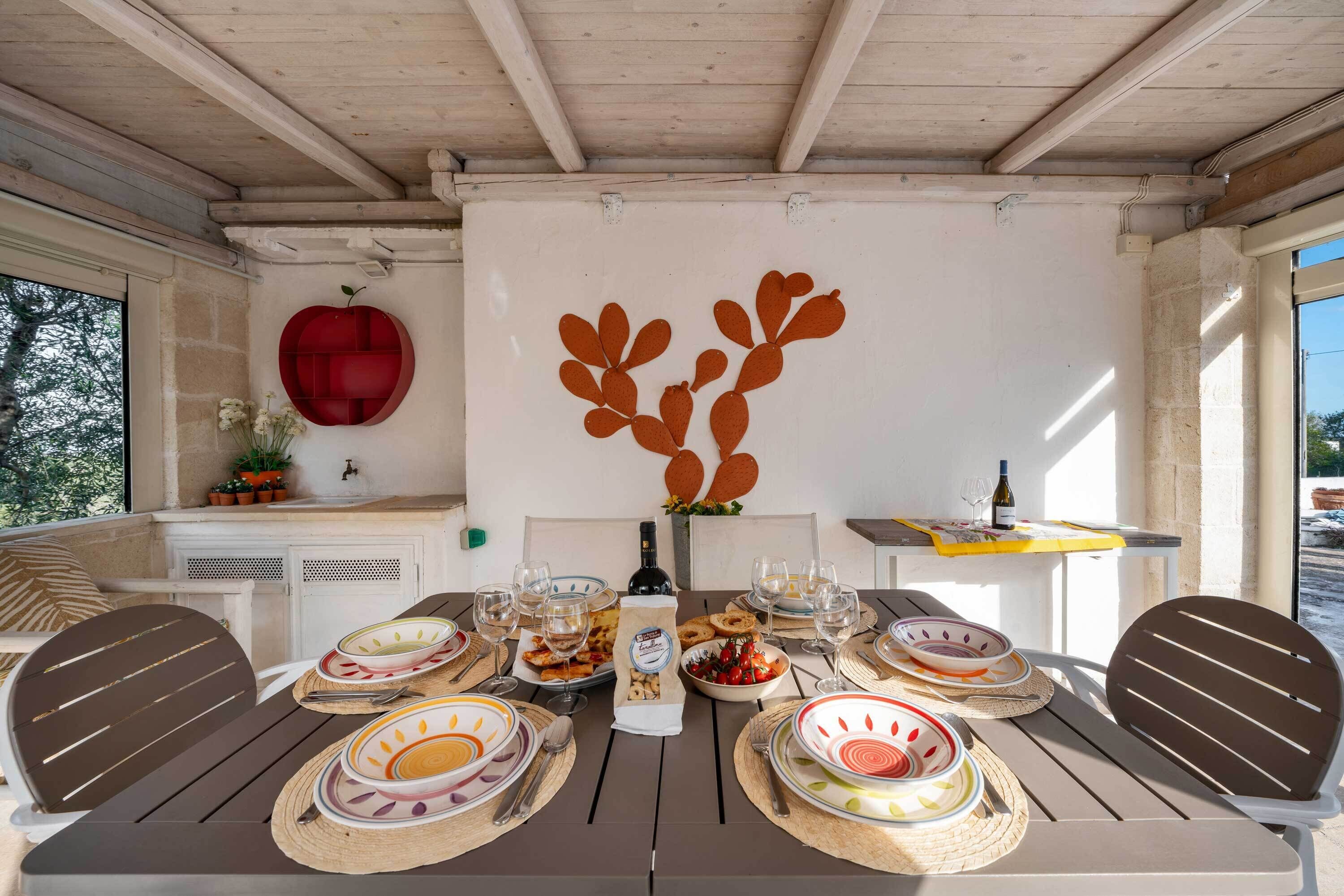 An outdoor dining area with a table set for a meal, surrounded by chairs, and a decorative wall with a red heart and leaf design.