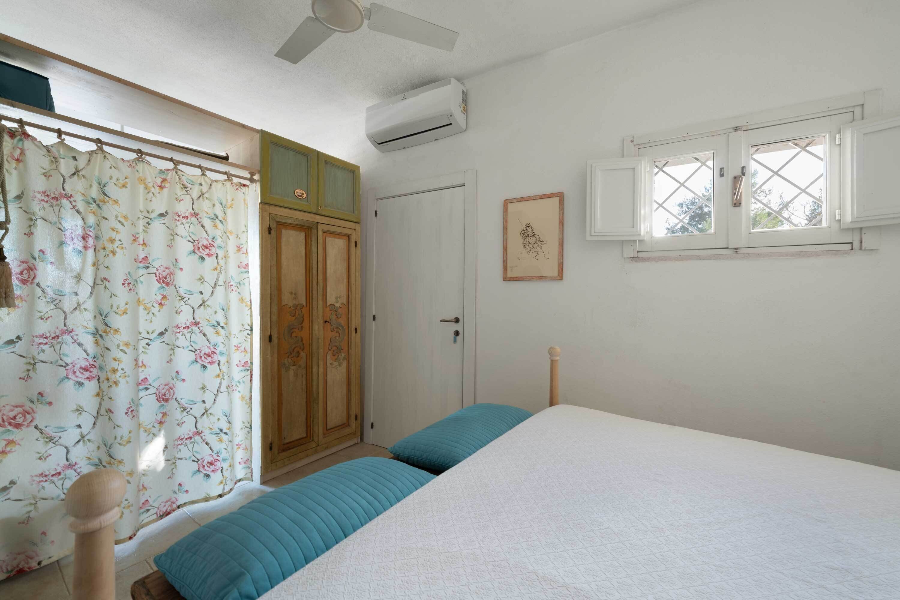 A bedroom with a bed, a window, an air conditioning unit, a door, and a curtain.