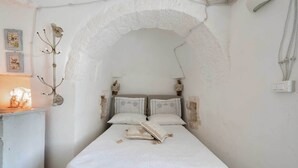 Un dormitorio con una cama blanca, dos almohadas, un libro abierto y un perchero decorativo.