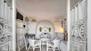Una habitación acogedora con una mesa y sillas de mimbre blanco, un pequeño arco blanco y un televisor en la pared.