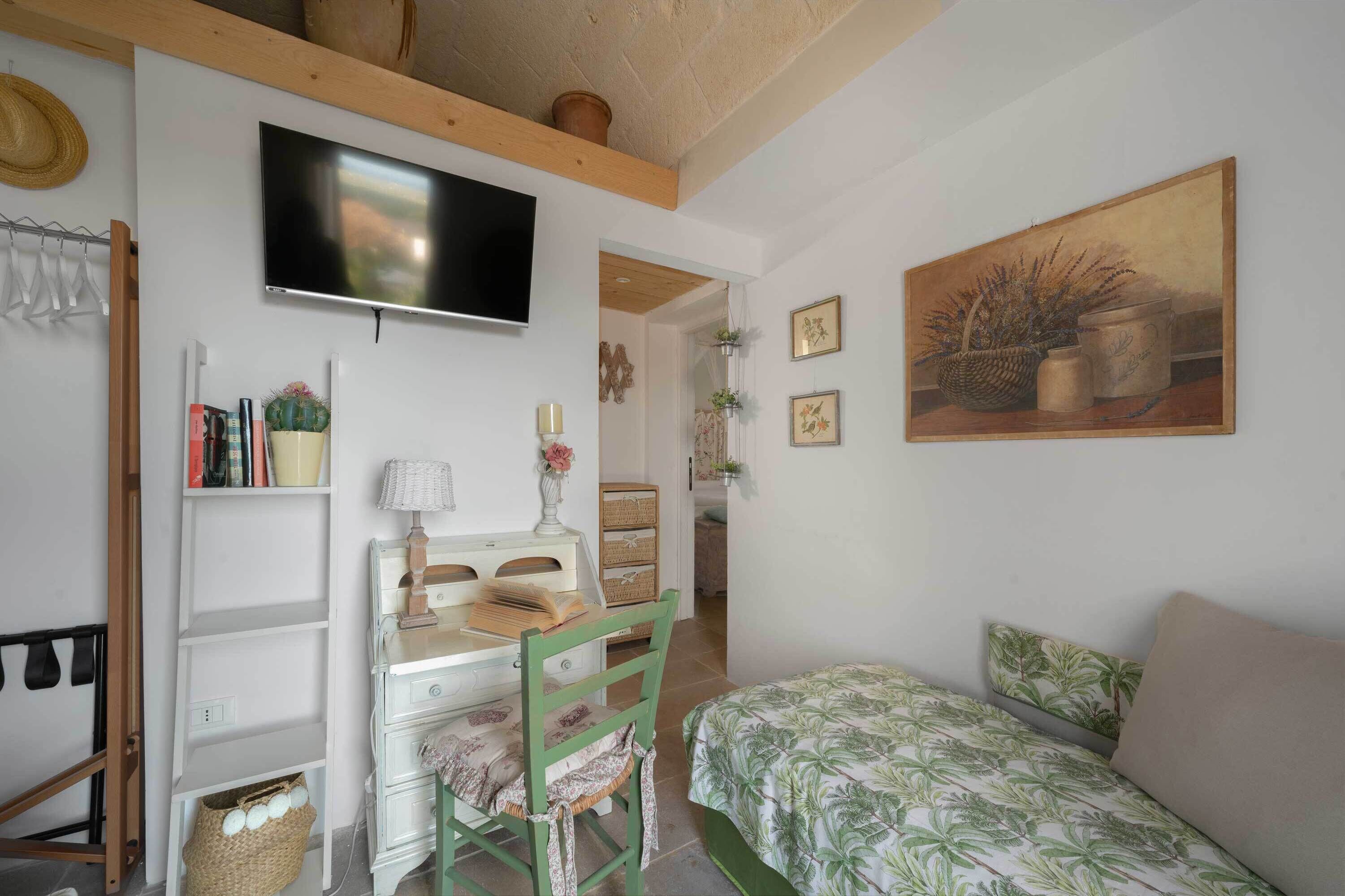 A cozy bedroom with a bed, a desk with a chair, a TV, and a painting on the wall.