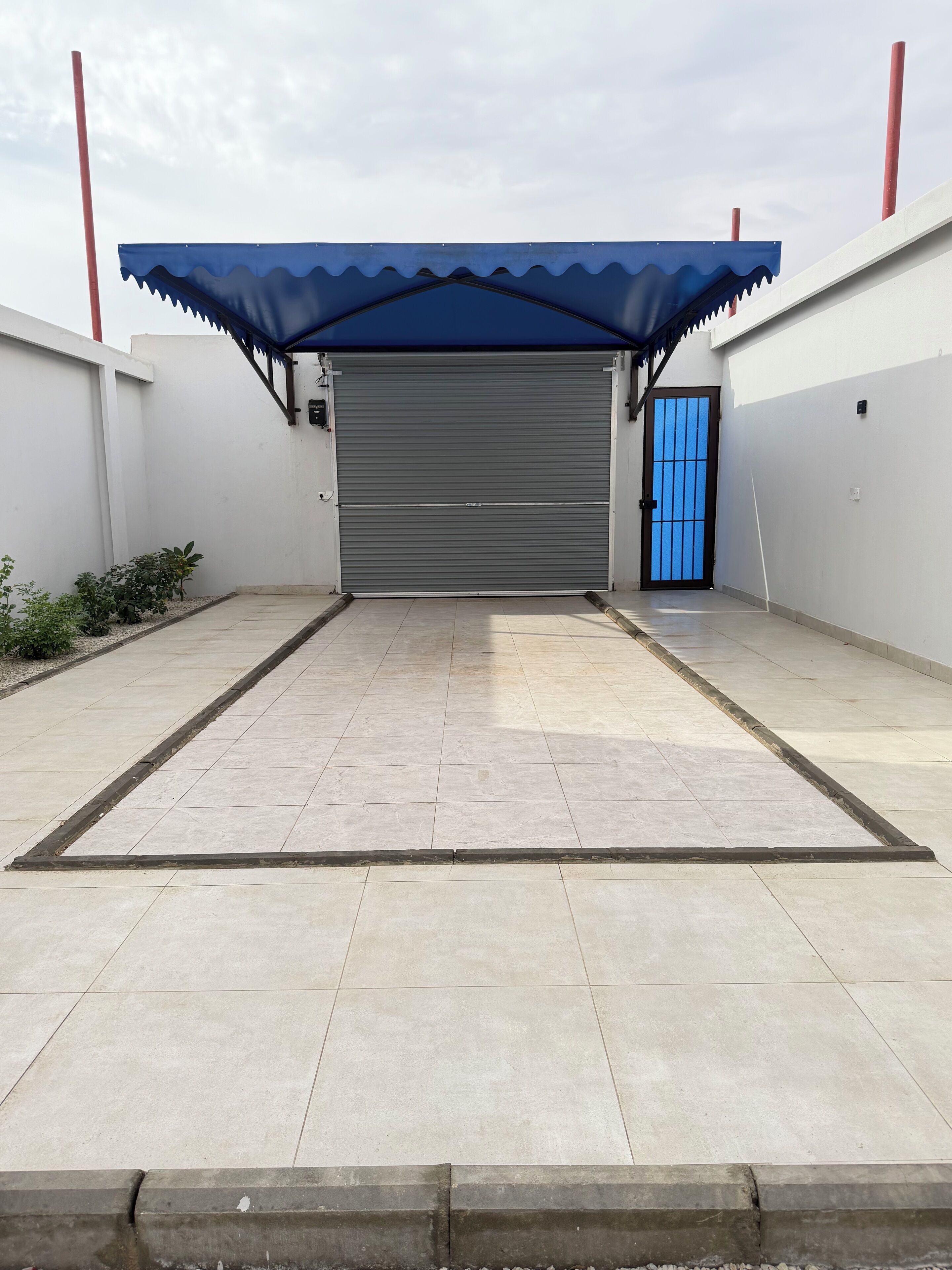 A covered loading dock with a closed garage door, a blue door, and a tiled floor.