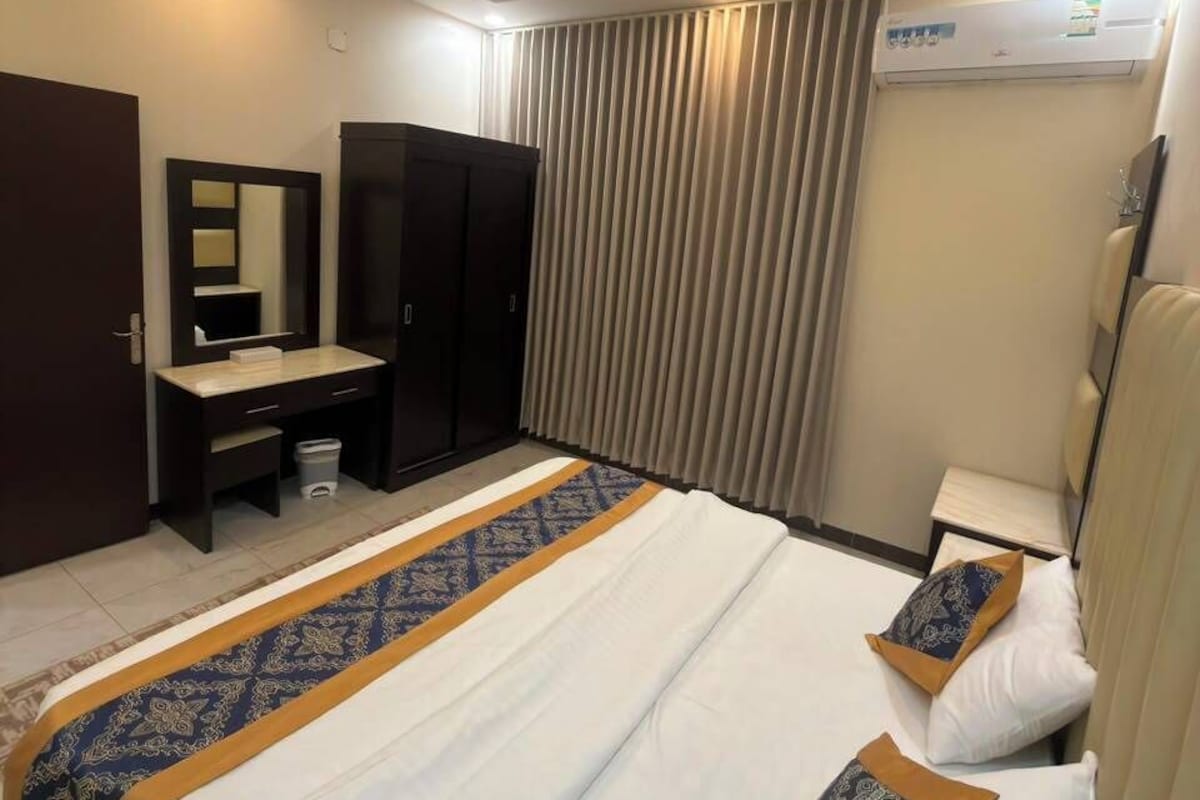 Quarto de hotel com uma cama, escrivaninha, guarda-roupa e espelho.
