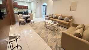 A modern living room with a beige sofa, a coffee table, and a dining area with chairs and a table. - تميُّز الاقامة للشقق المخدومة Tamyoz Aqama for Serviced Apartments (Ha'il)