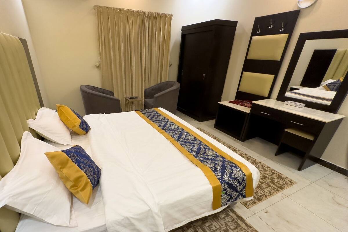 Quarto de hotel com cama, escrivaninha, cadeira, guarda-roupa e espelho.