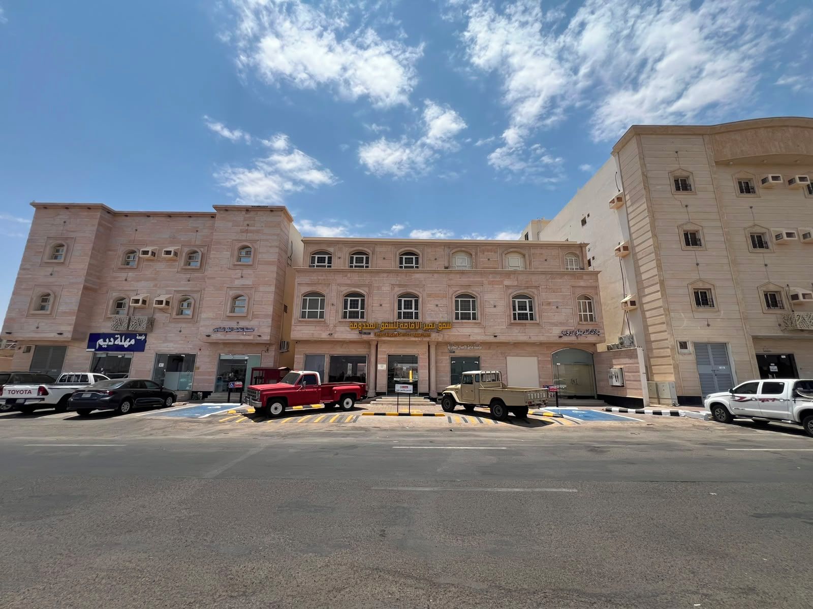 A multi-story building with a central entrance and a parking lot in front.
