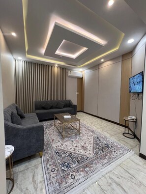 Uma sala de estar moderna com um sofá, mesa de centro, tapete estampado e uma televisão fixada na parede.