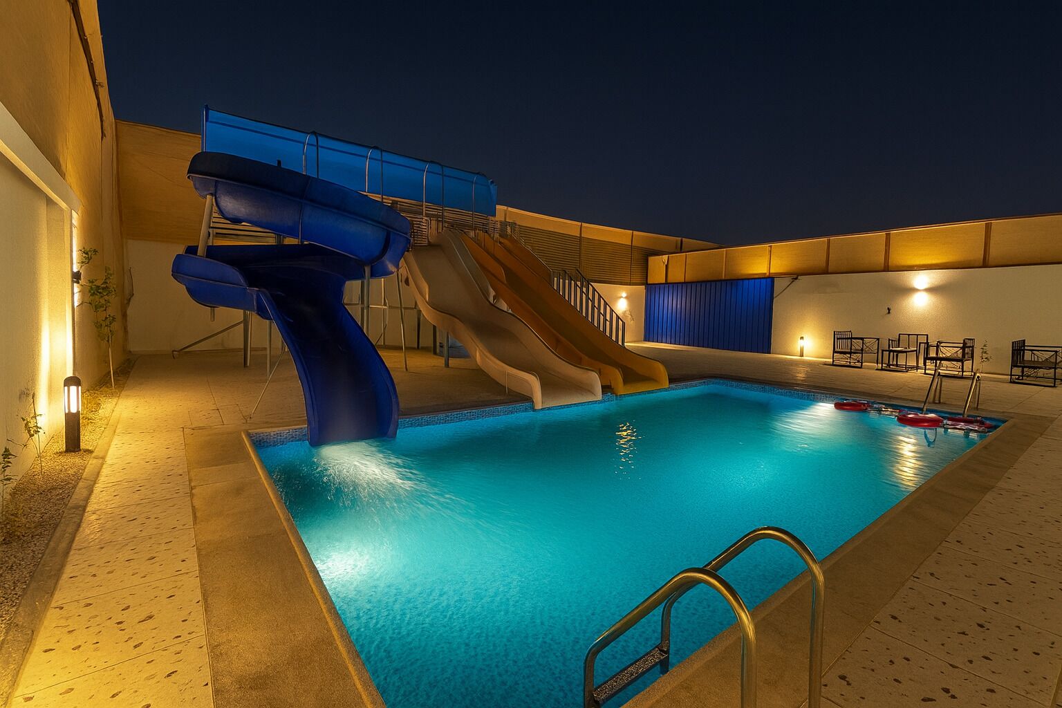 An indoor swimming pool with a water slide and a sun terrace with seating.