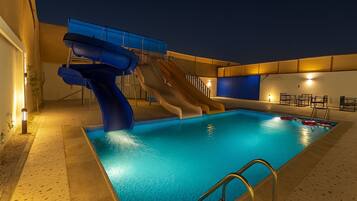 An indoor swimming pool with a water slide and a sun terrace with seating.