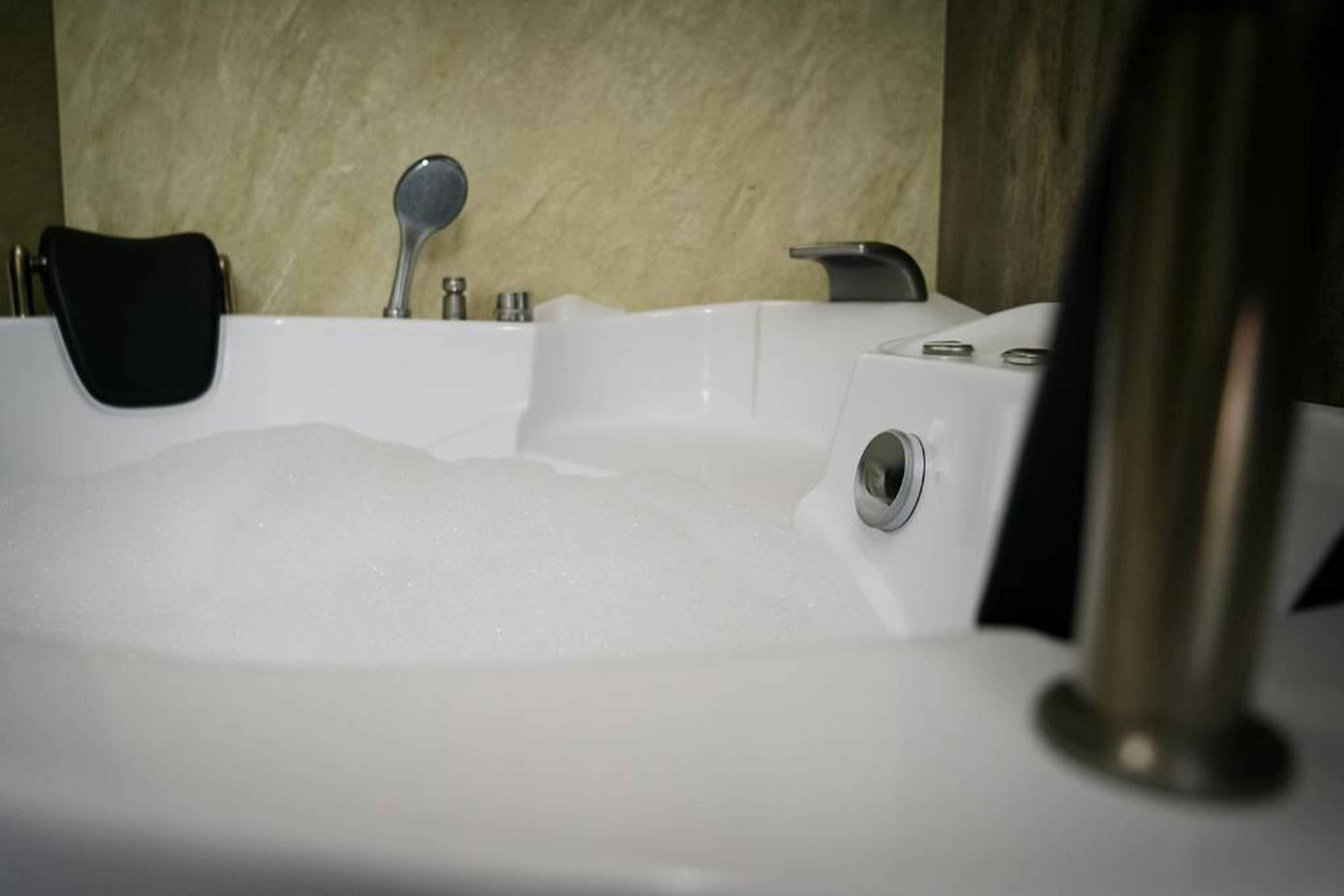 A bathtub filled with bubbles, a black chair, and a showerhead.