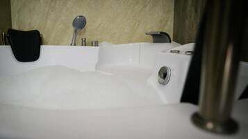 A bathtub filled with bubbles, a black chair, and a showerhead.