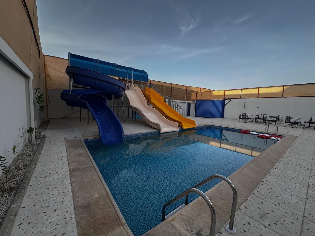 Una piscina con tobogán, zona techada y área de descanso.