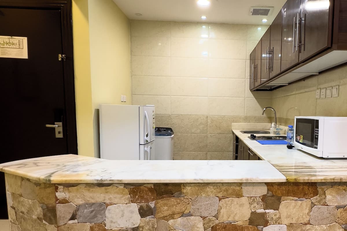 Cozinha com ilha de pedra, eletrodomésticos brancos e armários escuros.