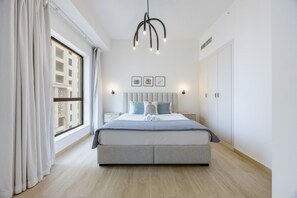 Un dormitori modern amb un llit gran, taules de nit, una làmpada penjant i una finestra amb cortines.