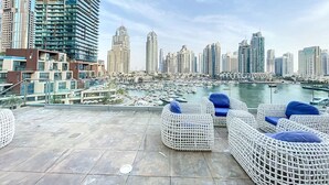 A rooftop terrace with white wicker furniture and a marina view. - Cayan Tower - Smart One Bedroom Loft on High Floor (Dubai Marina)