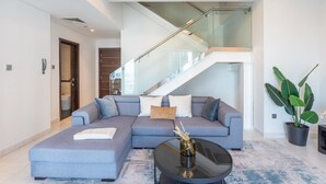 A modern living room with a grey sectional sofa, a glass staircase, and a potted plant. - Cayan Tower - Smart One Bedroom Loft on High Floor (Dubai Marina)