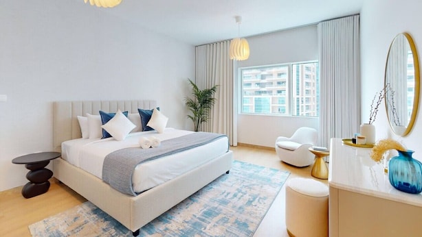 Un dormitorio moderno con una cama grande, una mesita de noche, una silla, un escritorio y un amplio ventanal con cortinas.