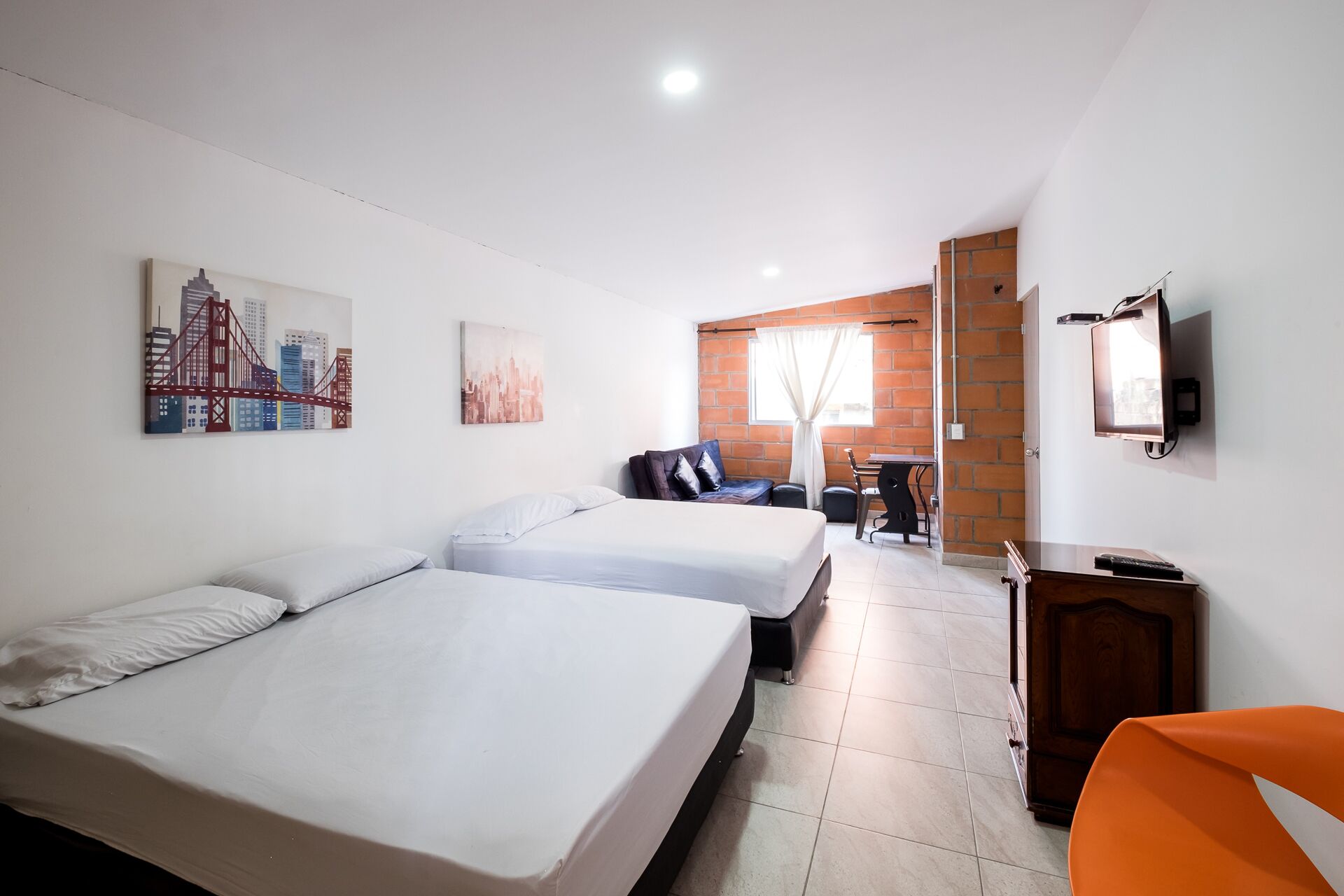 A hotel room with two beds, a desk, a chair, a TV, and artwork on the walls.