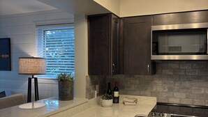 A modern kitchen with a marble countertop, dark cabinetry, a built-in oven, and a stainless steel microwave.
