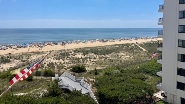 A beach view from a high-rise building with a flag, beach umbrellas, and a sandy shoreline. - 2 BR 2 BA Ocean Front building Pool and Tennis (Ocean City)