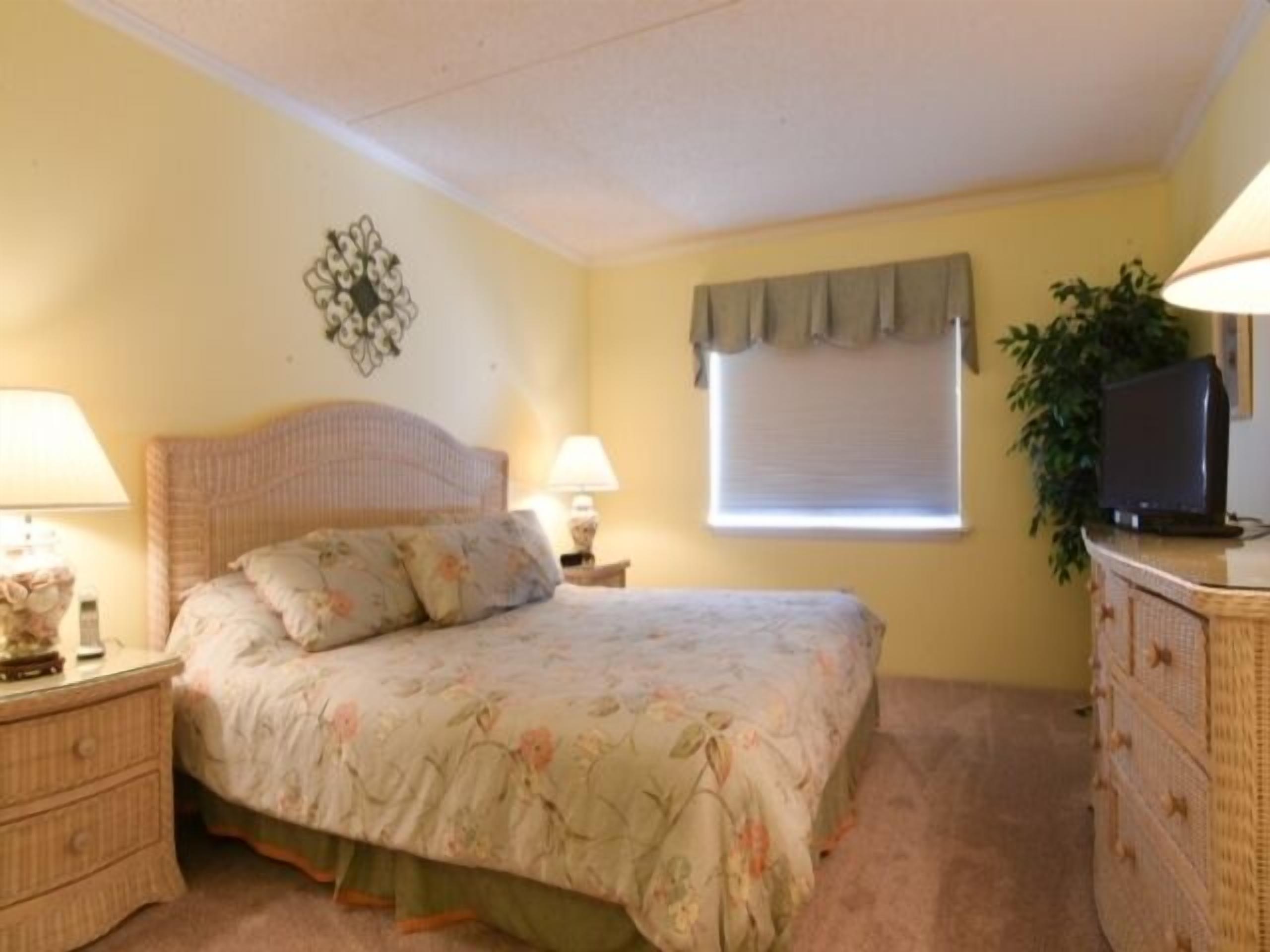 A bedroom with a bed, nightstands, a dresser, a television, and a window with a curtain.