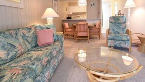 A living room with a floral sofa, a glass coffee table, and a dining area with wooden chairs. - 2 BR 2 BA Ocean Front building Pool and Tennis (Ocean City)