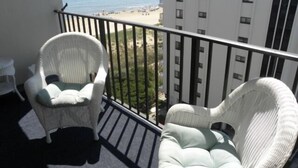 A balcony with two wicker chairs and a small table, overlooking a beach and high-rise buildings. - 2 BR 2 BA Ocean Front building Pool and Tennis (Ocean City)