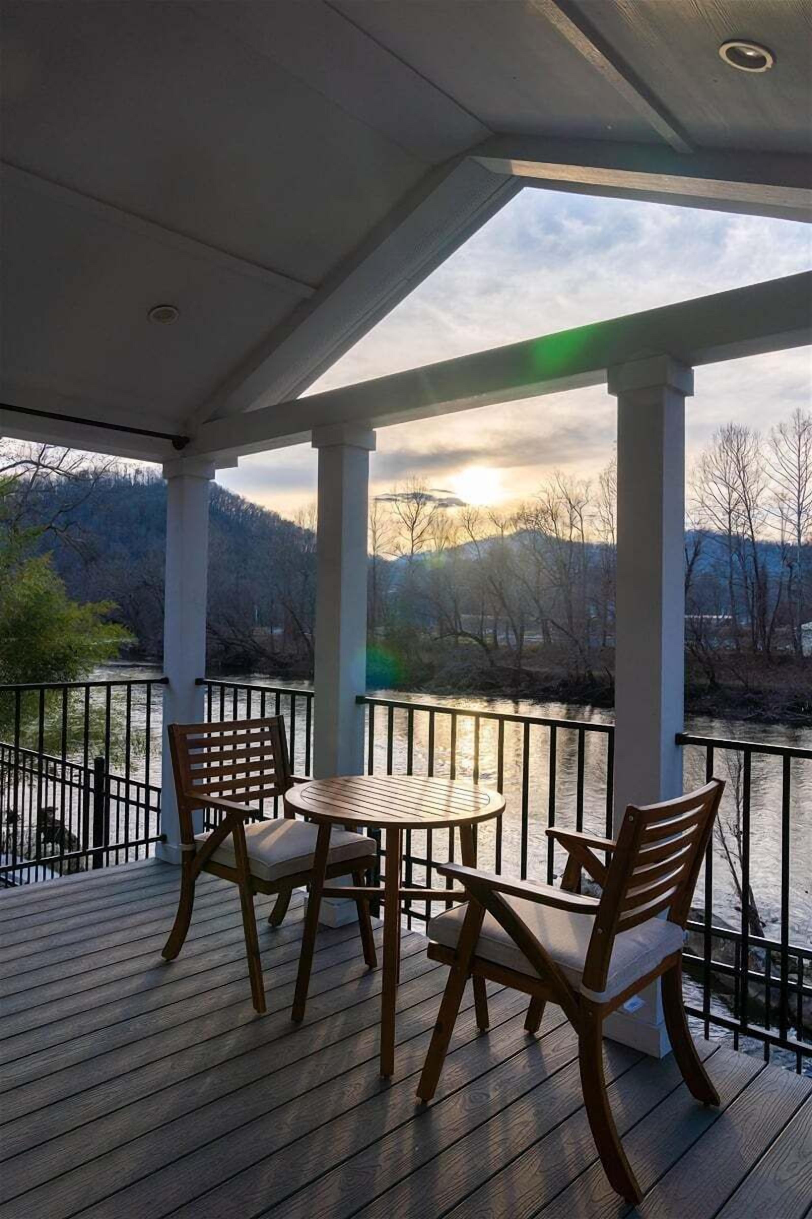 Un espacio al aire libre techado con una mesa y sillas, con vistas a un río y montañas.