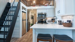 Una cocina moderna con una isla central, electrodomésticos de acero inoxidable y una escalera de madera.