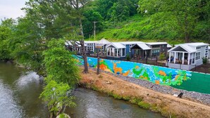 A riverside property with a colorful mural, wooden cabins, and lush greenery.