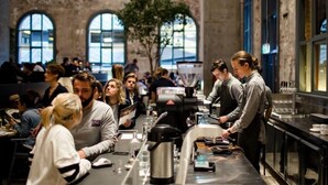 A busy café with patrons seated at tables, a barista preparing drinks, and a large coffee machine.