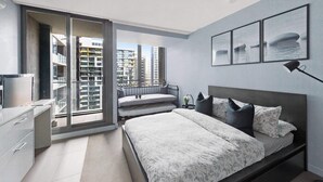 A modern bedroom with a large bed, a nightstand, a desk, and a view of the city through a sliding door.