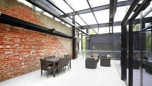 A modern outdoor patio with a brick wall, glass enclosure, and outdoor furniture.
