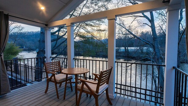 A covered outdoor area with a wooden deck, two wooden chairs, and a small round table.