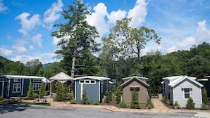 A row of mobile homes with a gravel driveway and picnic tables, surrounded by trees and a clear sky.