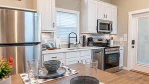 A modern kitchen with white cabinets, stainless steel appliances, and a wooden island with a bowl and cutlery.