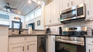 Una cocina moderna con armarios blancos, electrodomésticos de acero inoxidable y un ventilador de techo estilo campestre.