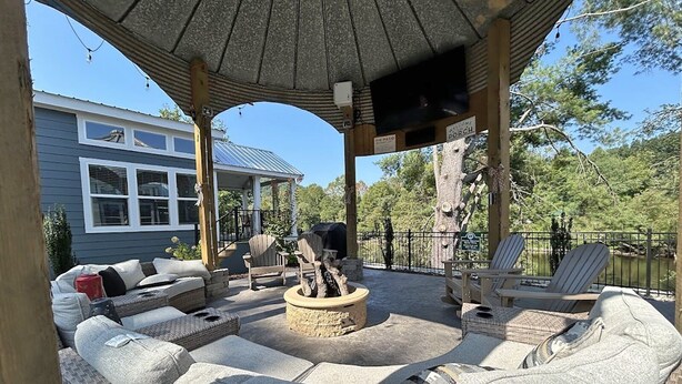 Un espacio de estar al aire libre con techo, mobiliario de mimbre, una chimenea y una pantalla de televisión.