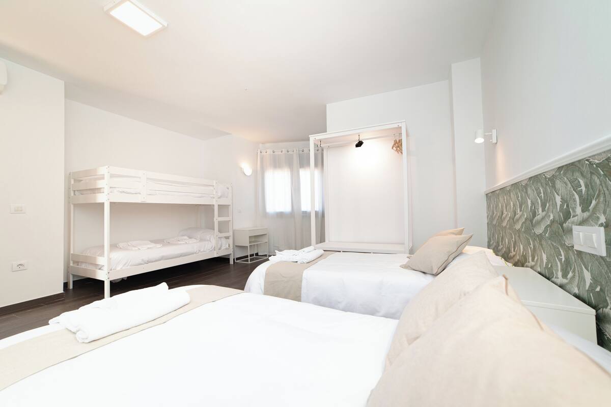 A hotel room with two beds, a bunk bed, a desk, and a shower area.